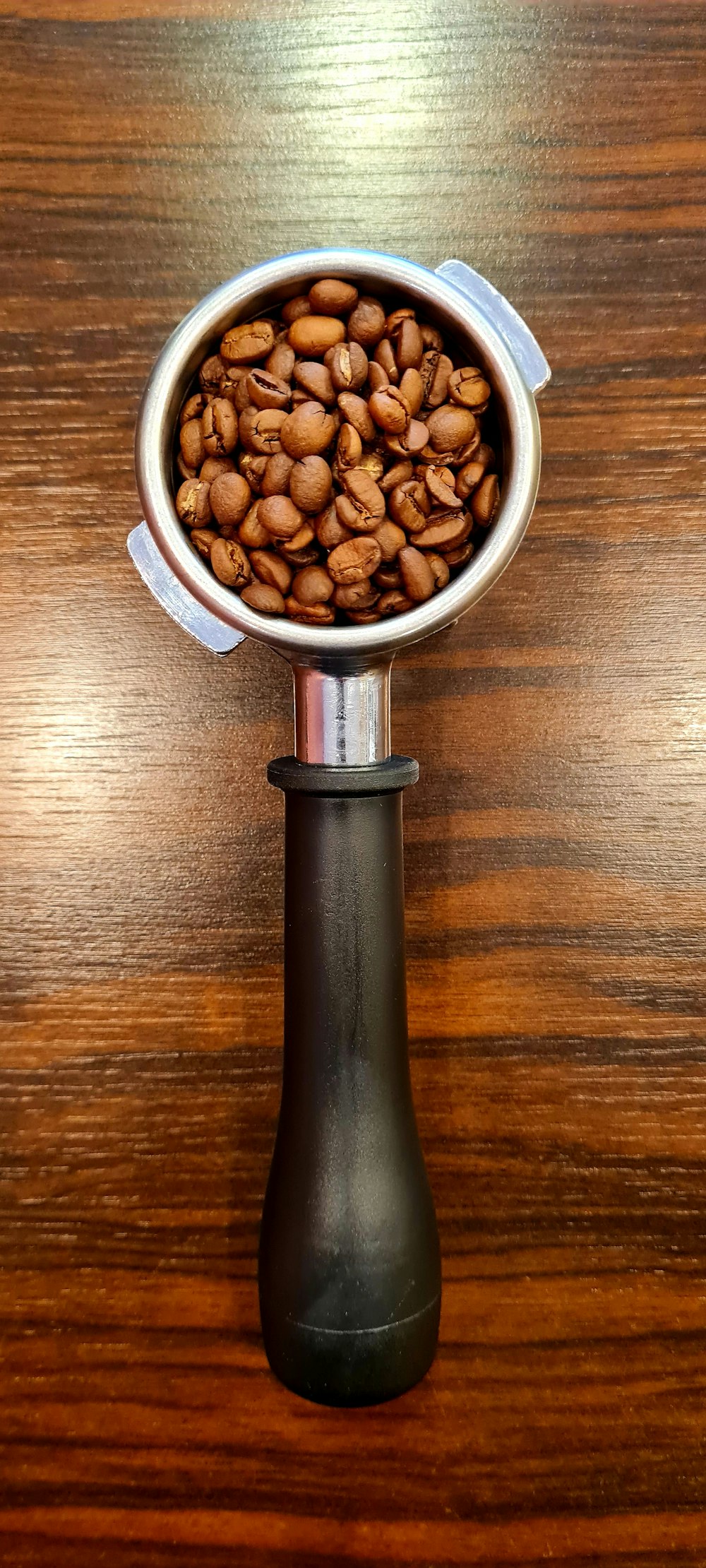 uma xícara de metal cheia de grãos de café em cima de uma mesa de madeira