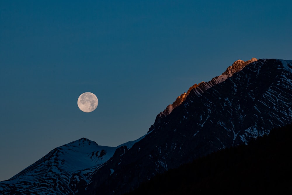 a full moon rising over a mountain range