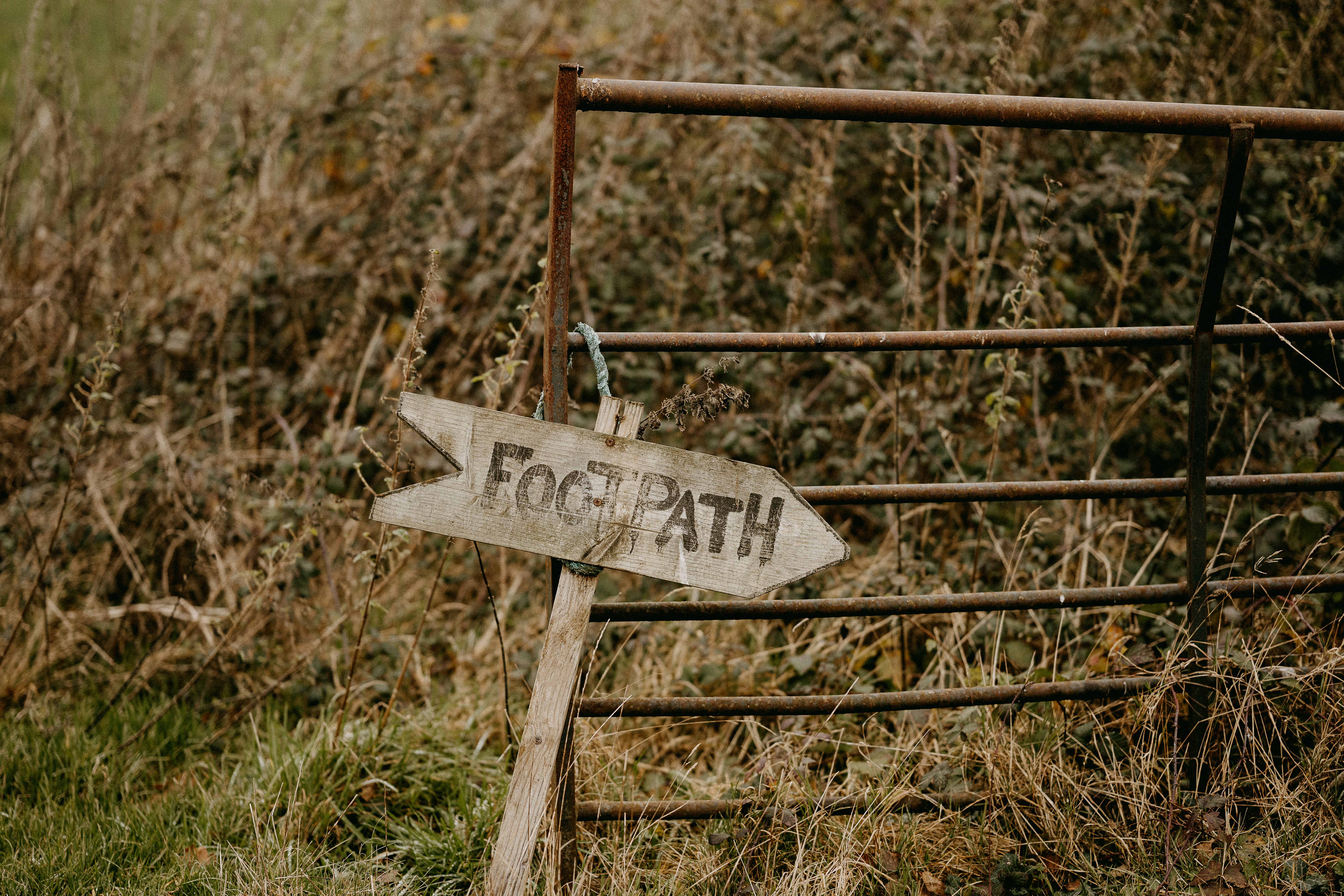 a wooden sign pointing to the right in front of a fence