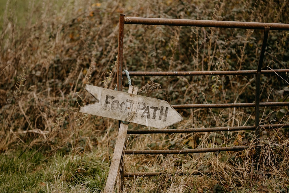 a wooden sign pointing to the right in front of a fence