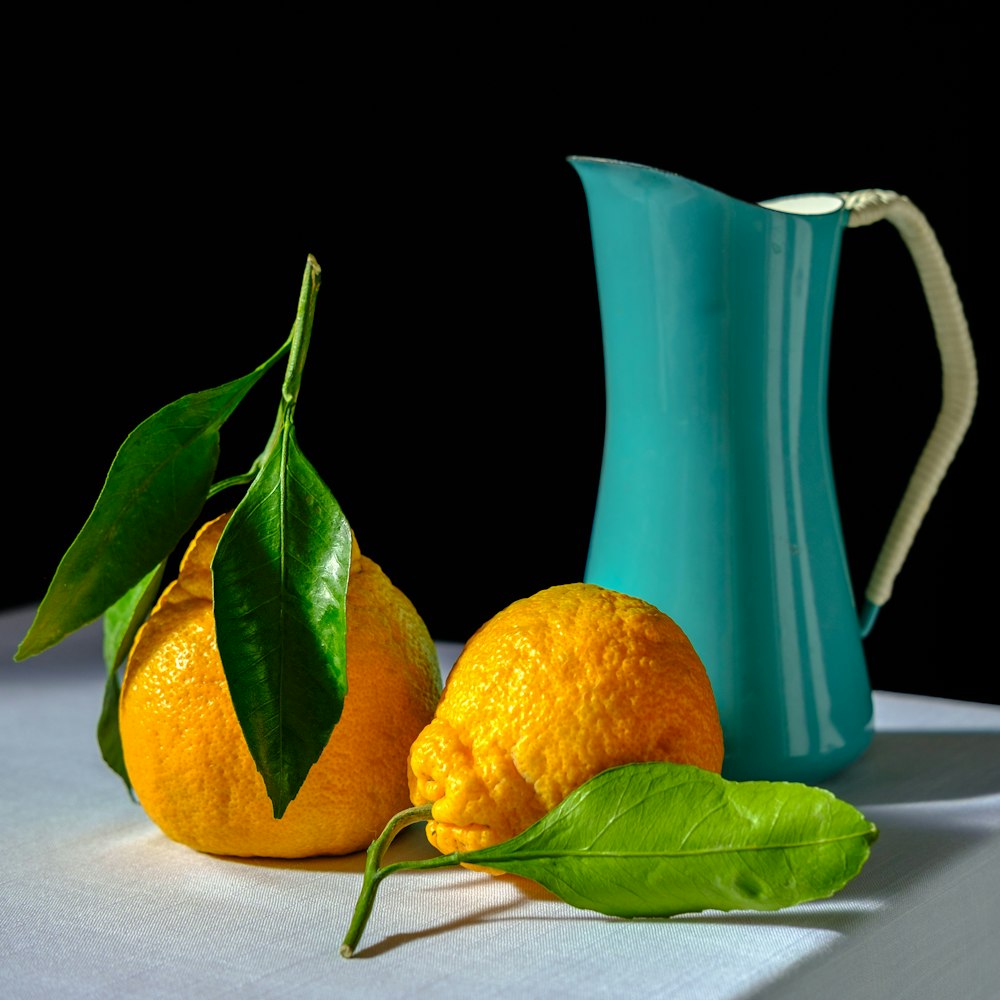 Dos naranjas y una jarra azul sobre una mesa