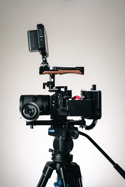 A professional camera setup mounted on a tripod, featuring a large lens and an external monitor attached above the camera body. The setup includes various accessories, such as a wooden handle and cables connected to the camera.