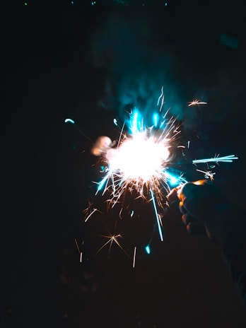 Hands holding a sparkler glowing brightly against a dark background.