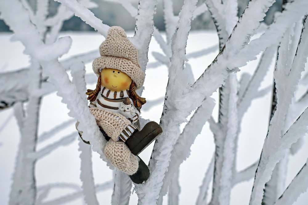 um bicho de pelúcia sentado em cima de uma árvore coberta de neve