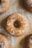 Several baked donuts are arranged on a surface, sprinkled with a light dusting of powdered sugar. The donuts have a golden brown color and appear freshly baked, with a soft texture visible on their surface.