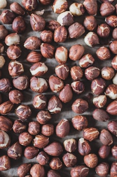 A collection of brown and beige hazelnuts spread out, showcasing a mix of whole nuts and some with their shell partially removed.