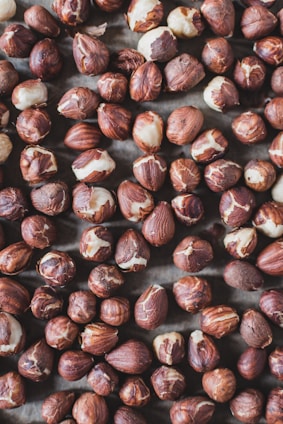 A collection of brown and beige hazelnuts spread out, showcasing a mix of whole nuts and some with their shell partially removed.