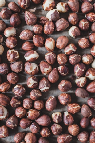 A handful of mixed nuts including hazelnuts, pine nuts, and almonds with pistachio tones in the background.