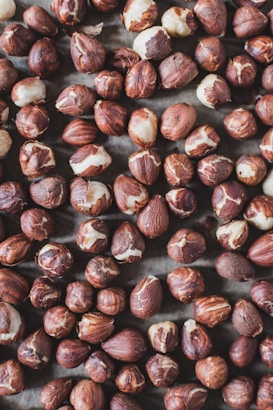 A collection of brown and beige hazelnuts spread out, showcasing a mix of whole nuts and some with their shell partially removed.