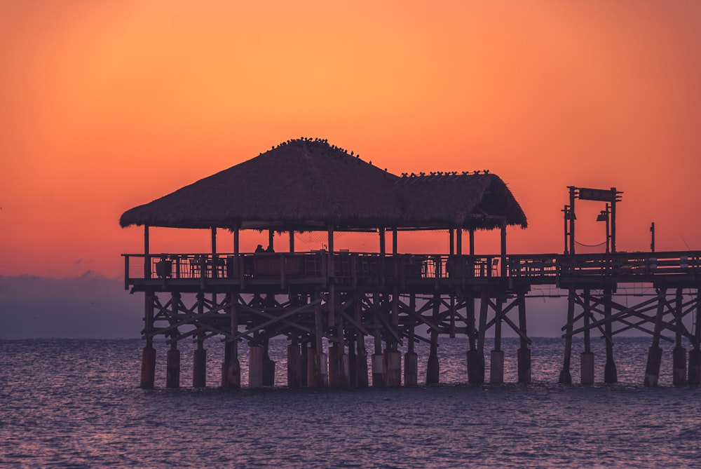 a pier with a thatched roof at sunset