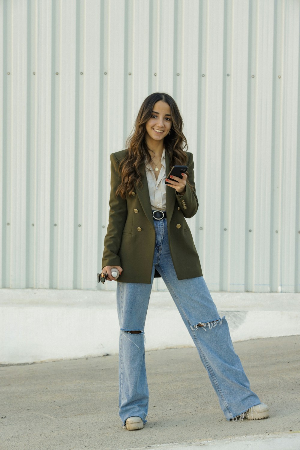 a woman in a green jacket and jeans looking at her cell phone