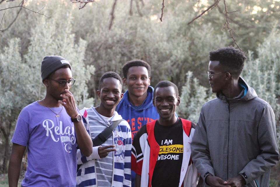 Five young men stand together, each holding up their phone to take a photo
