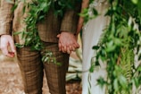 The couple holding hands against a backdrop of burgundy drapes and soft greenery.