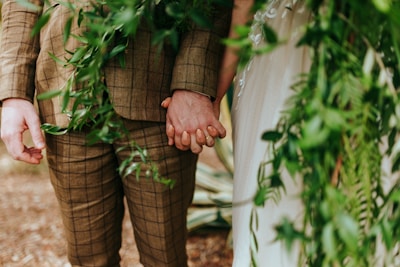 The couple holding hands against a backdrop of burgundy drapes and soft greenery.