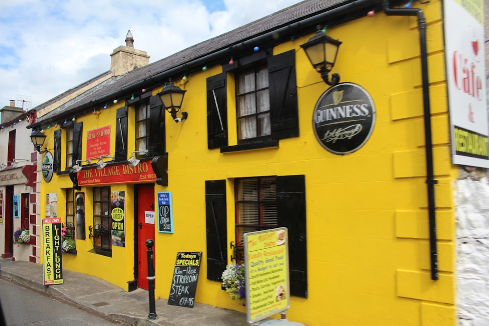 a yellow building with black shutters and signs on it