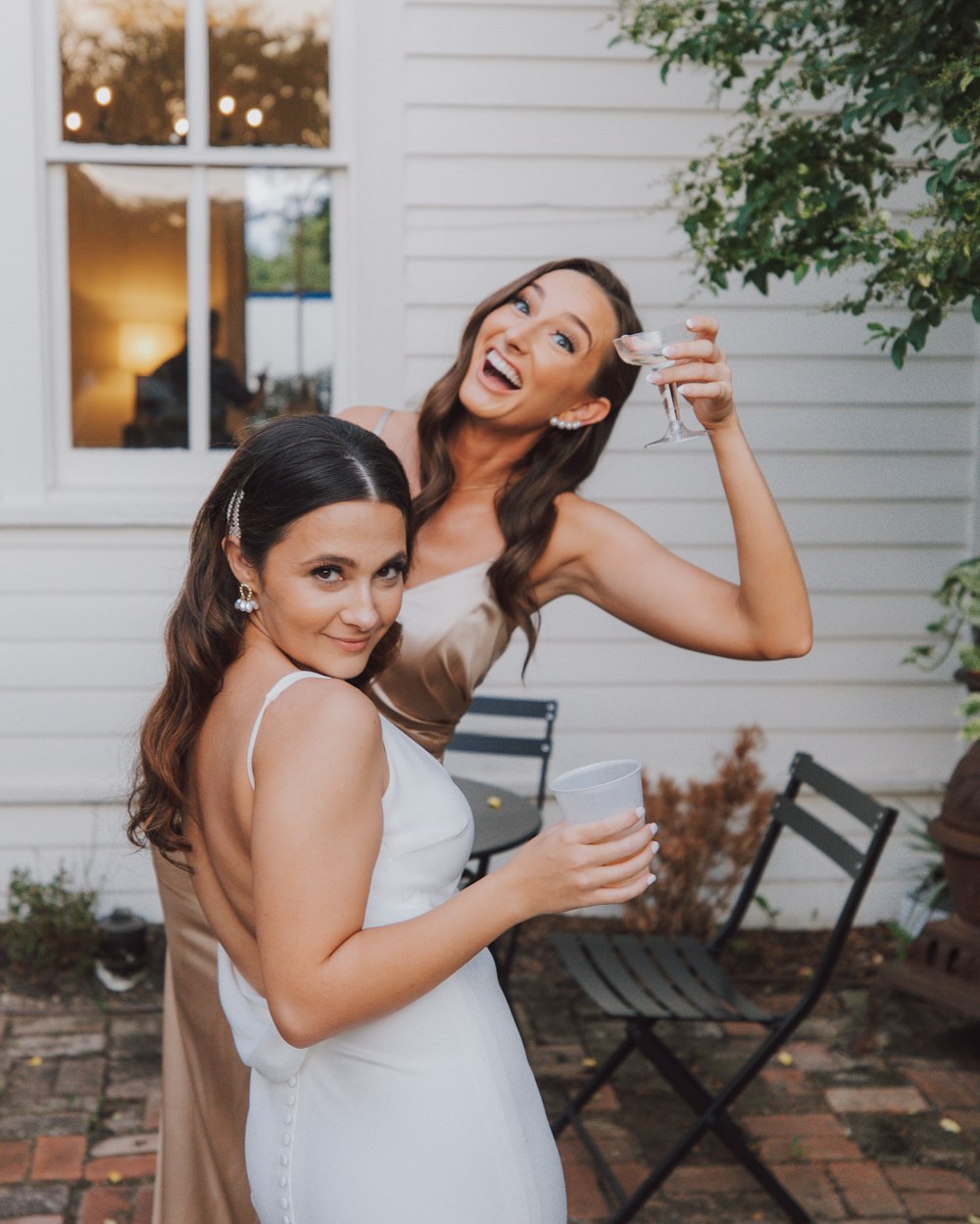 two women standing next to each other in front of a house