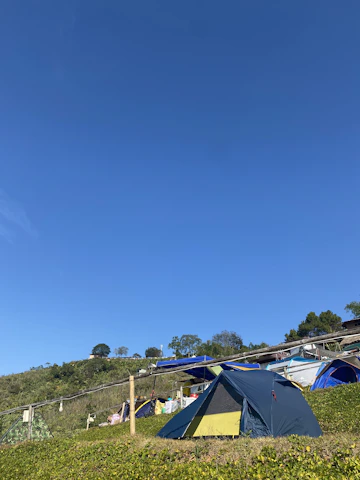 A vibrant outdoor scene showing hikers gearing up with backpacks and tents under a clear blue sky.