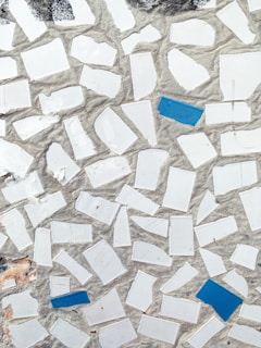 A mosaic pattern featuring irregularly shaped white tiles with scattered blue tiles set in a cement background. The texture gives a rough, handcrafted appearance with natural wear visible.