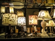 A collection of decorative table lamps displayed on a glass shelf, featuring shades adorned with intricate bird and butterfly patterns. The warm glow casts an inviting ambiance.