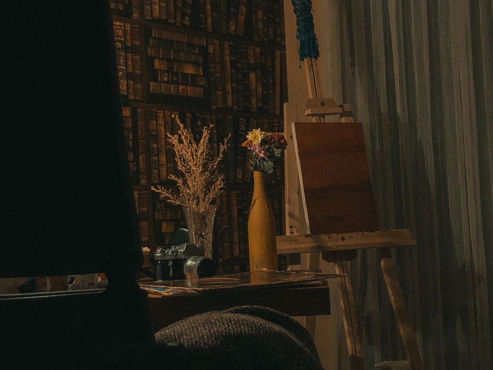 a table with a vase of flowers next to a painting easel