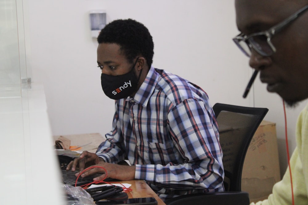 a man sitting at a desk wearing a face mask