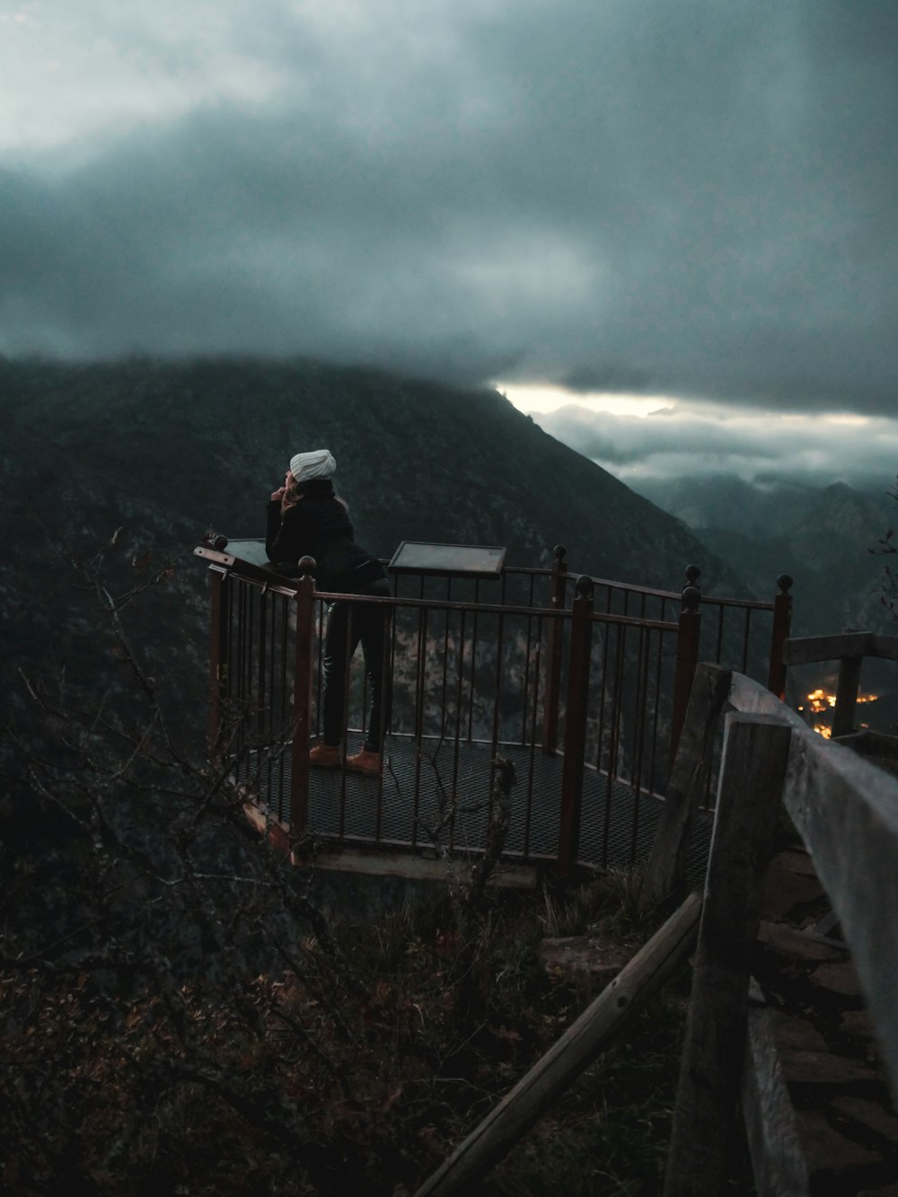 a person sitting on a railing overlooking a mountain