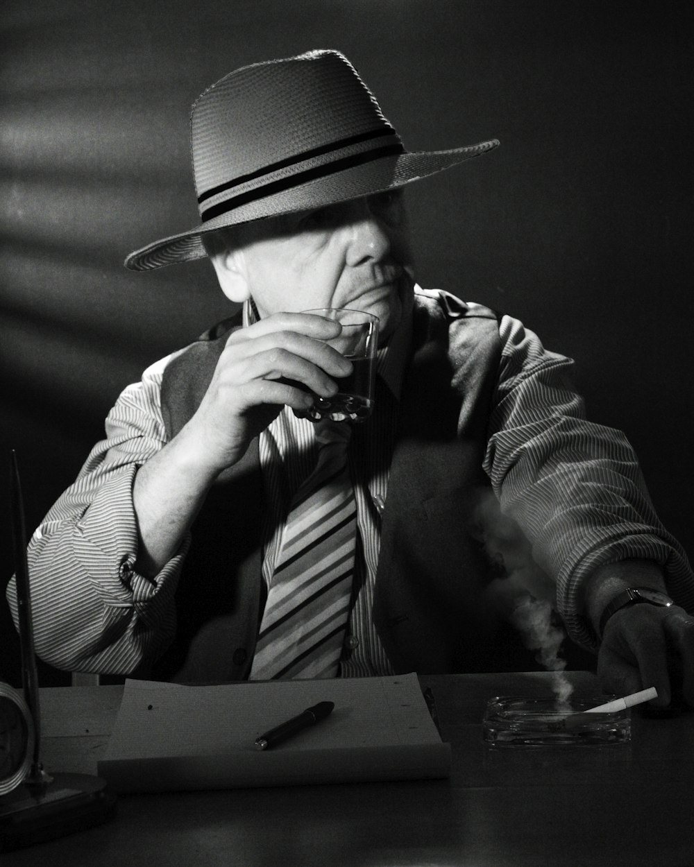 a man wearing a hat and tie sitting at a desk