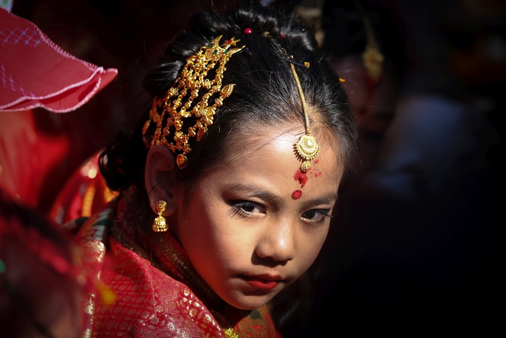 a young girl wearing a red and gold head piece
