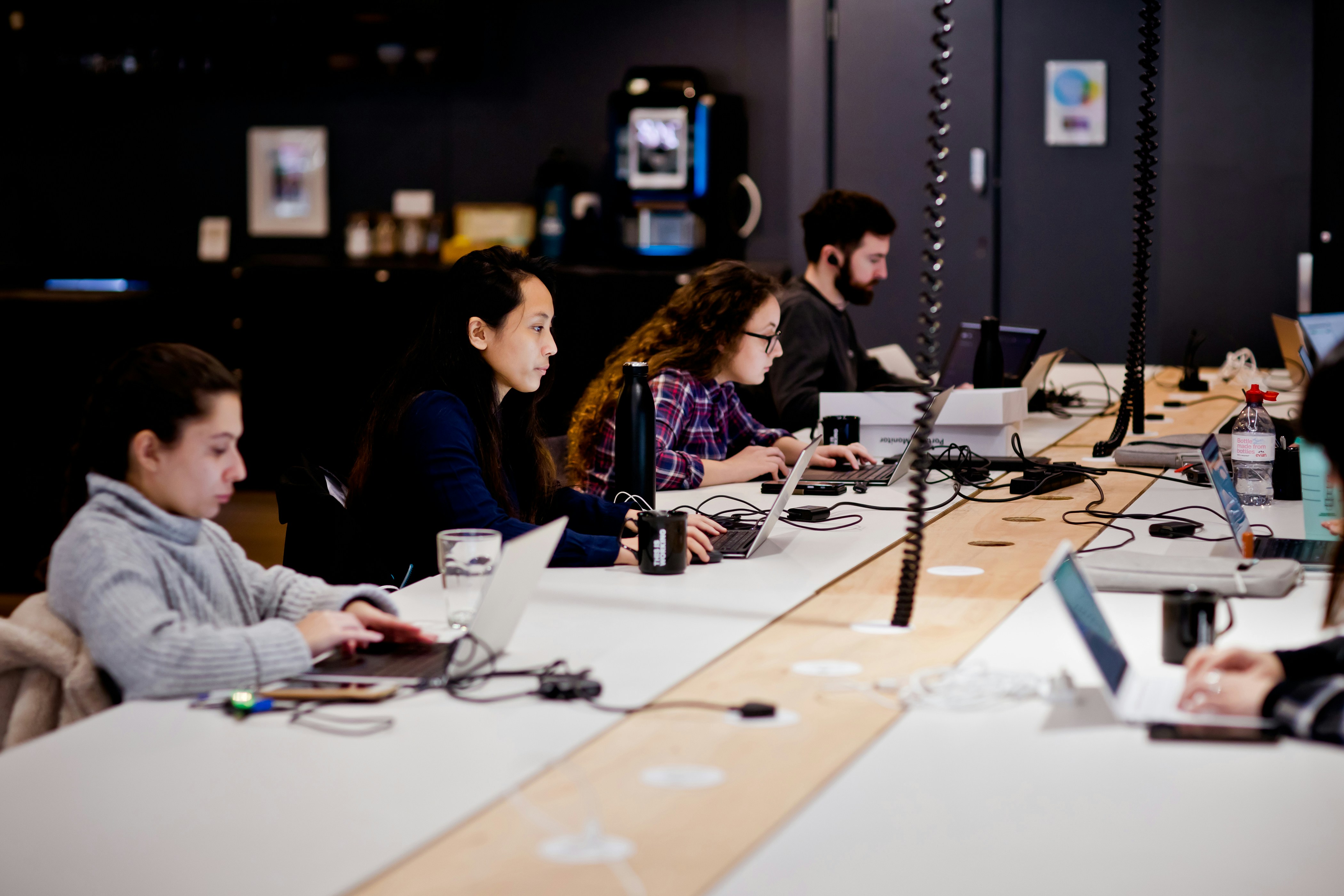 a group of people sitting at a table with laptops, 