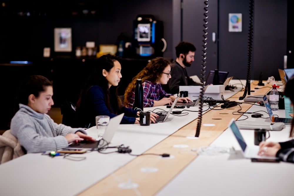 a group of people sitting at a table with laptops