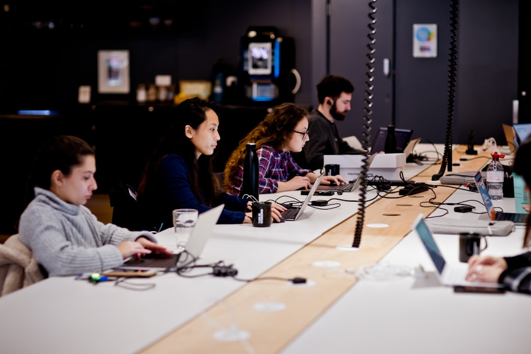 a group of people sitting at a table with laptops,