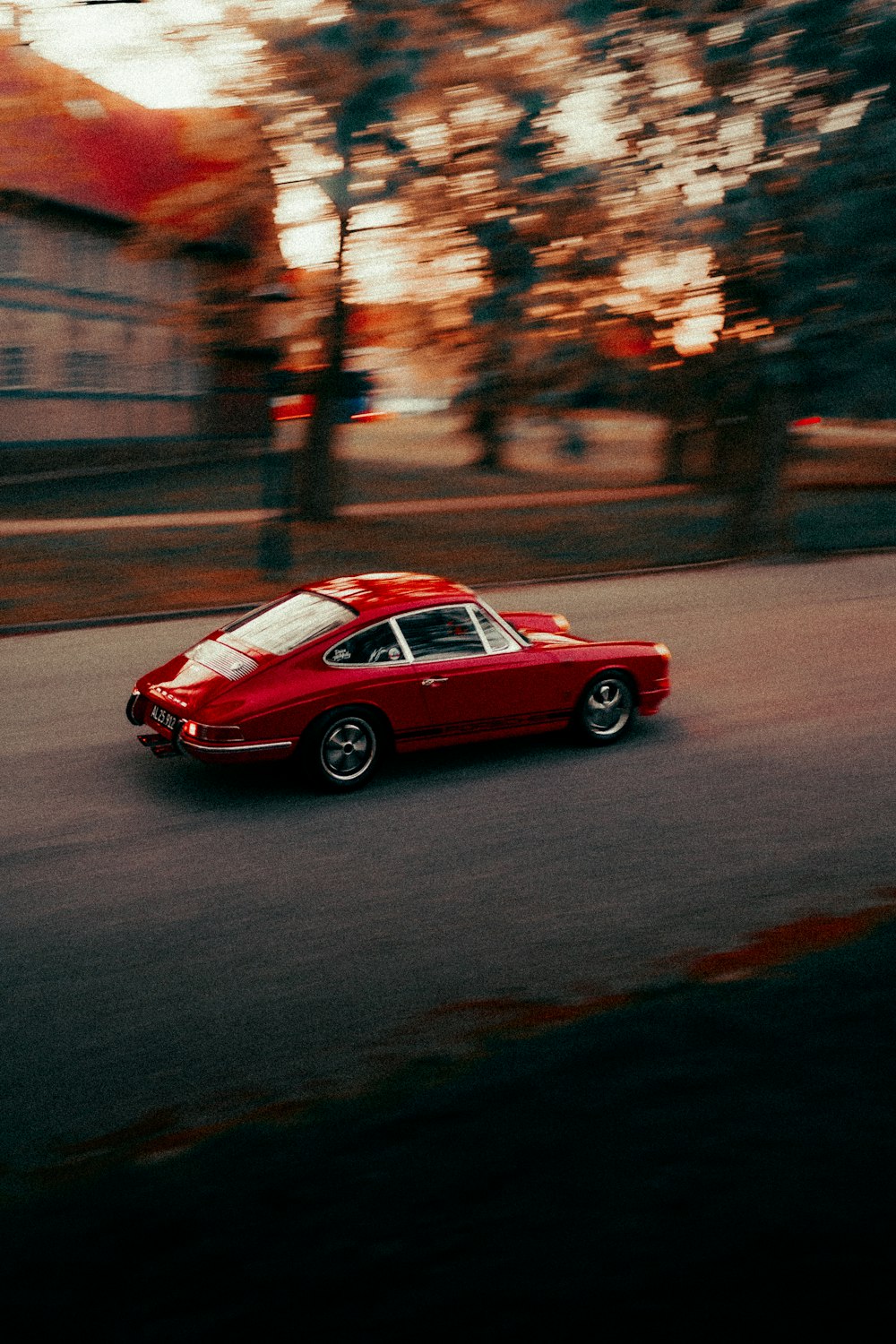 a red car driving down a street next to trees