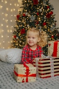 a little girl sitting on a bed next to presents