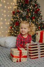 a little girl sitting on a bed next to presents