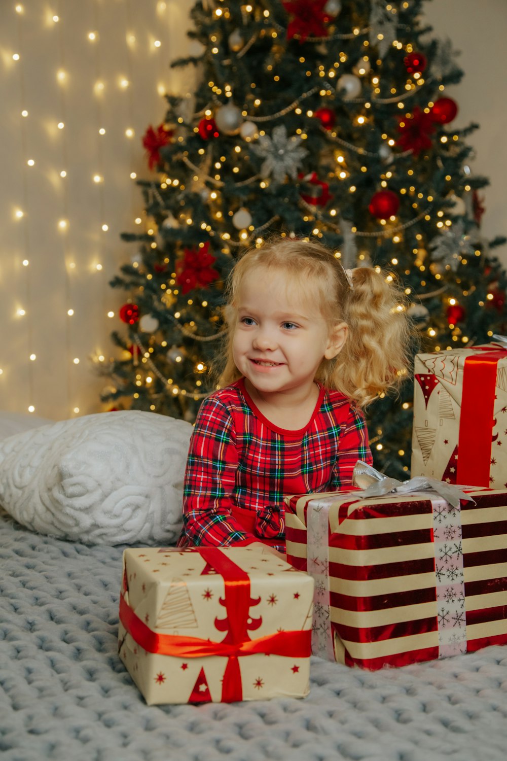 a little girl sitting on a bed next to presents