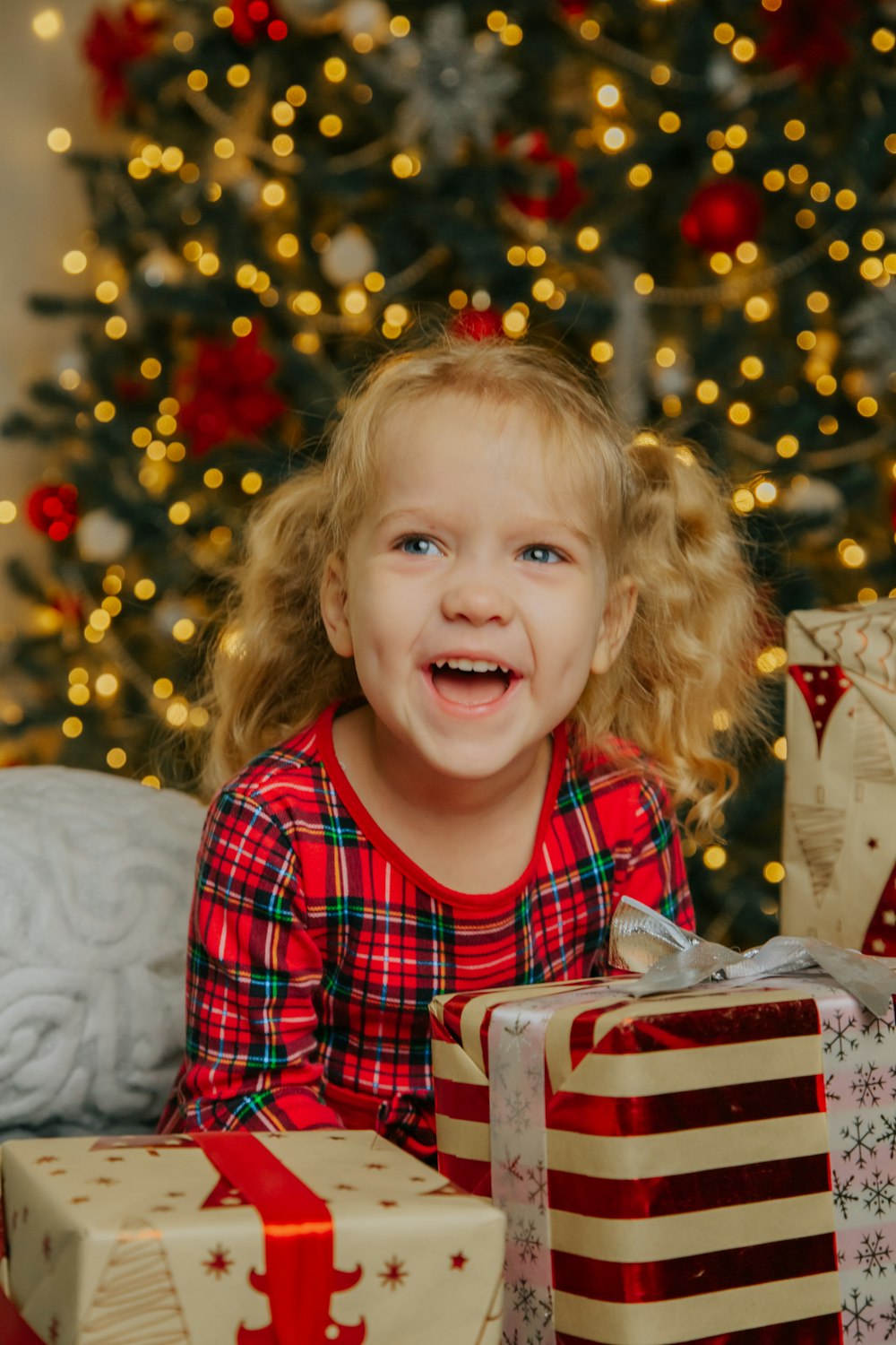 Une petite fille assise devant un sapin de Noël avec des cadeaux