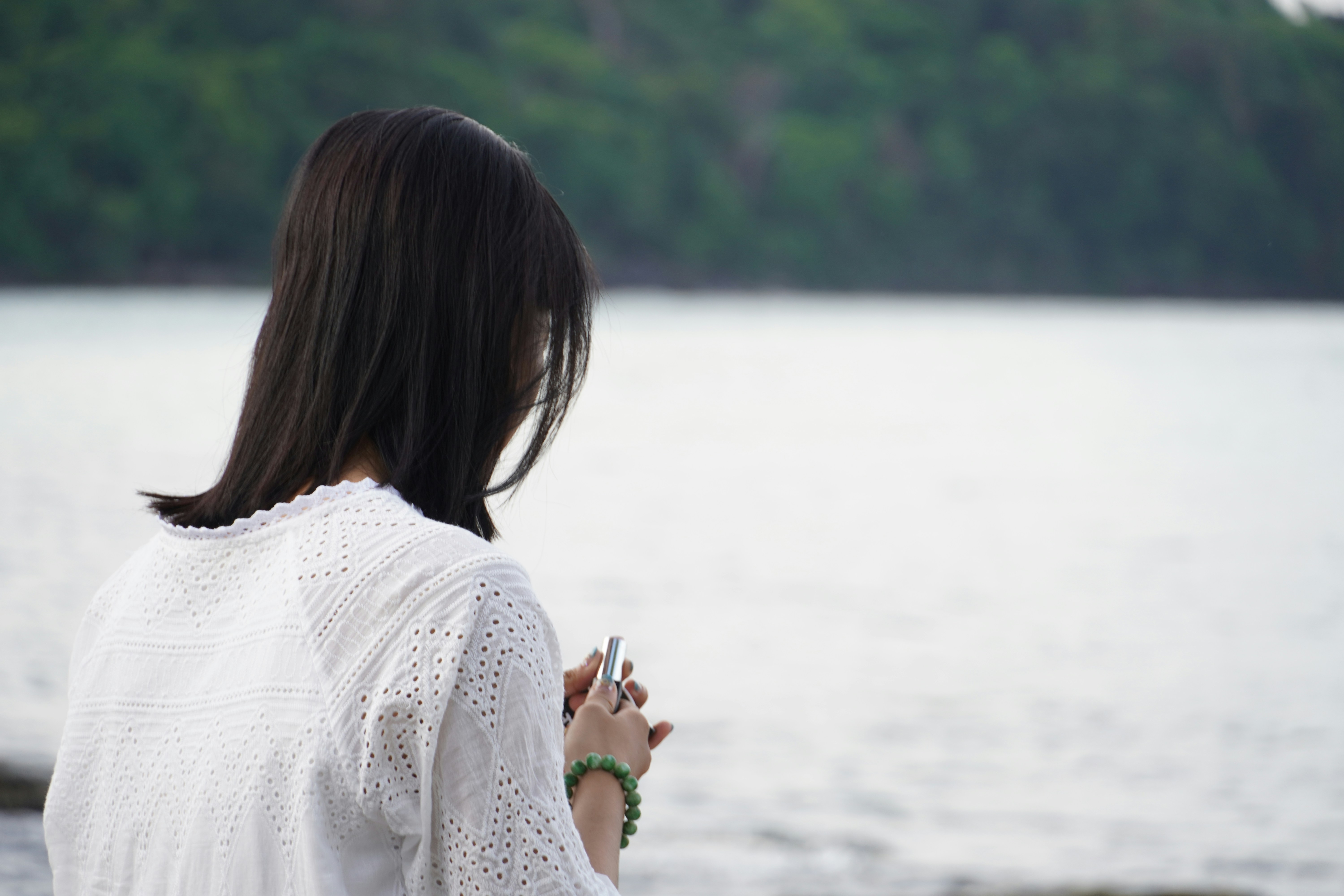 a woman holding a cell phone standing next to a body of water