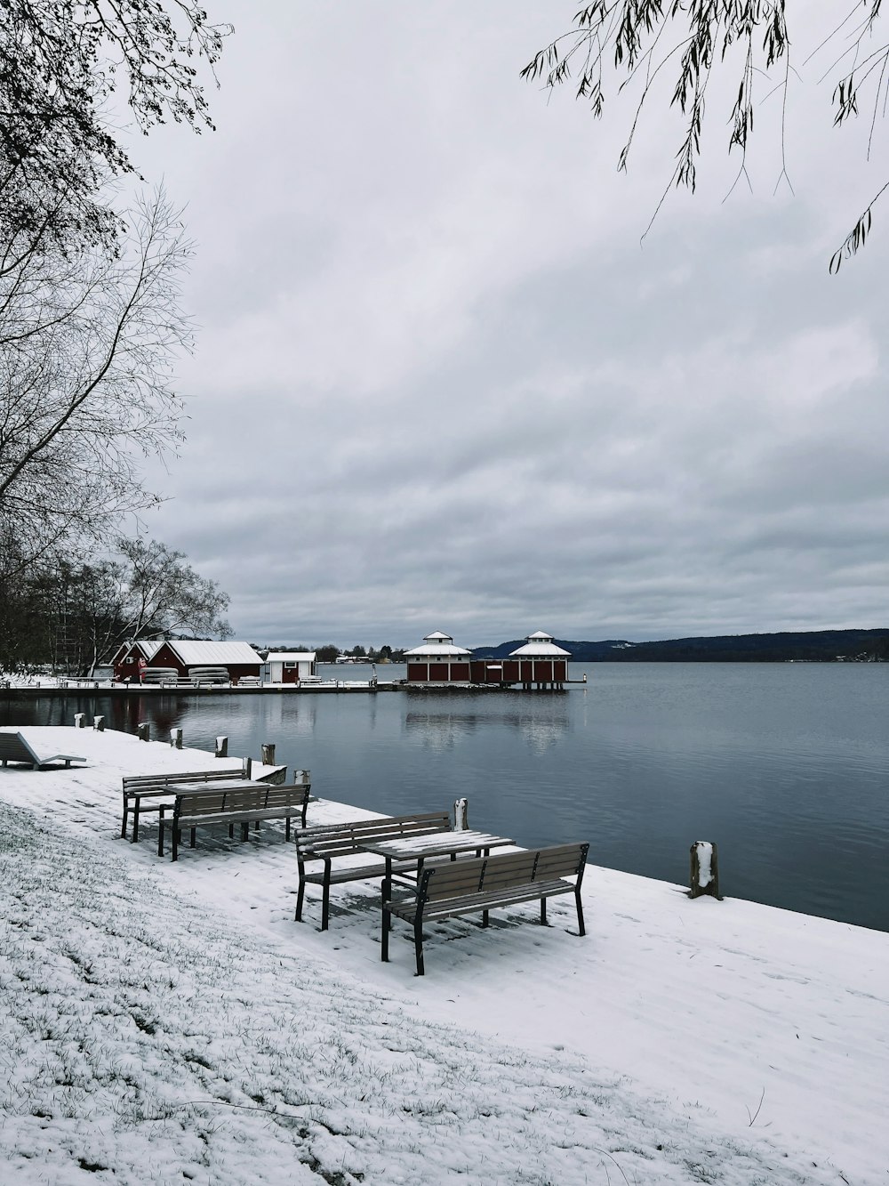 a row of benches sitting next to a lake covered in snow