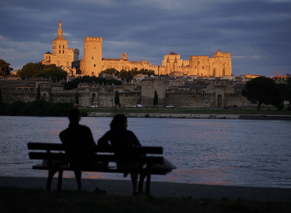 two people sitting on a bench near a body of water