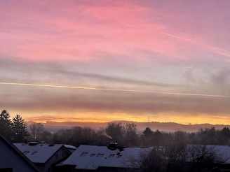A wide-angle shot of a sky streaked with dense, white chemtrails over a suburban neighborhood at sunset