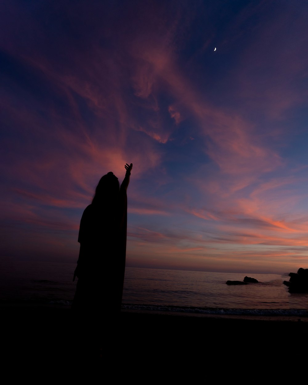 Eine Person, die an einem Strand mit einem Sonnenuntergang im Hintergrund steht