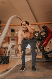 a shirtless man holding a rope in a gym