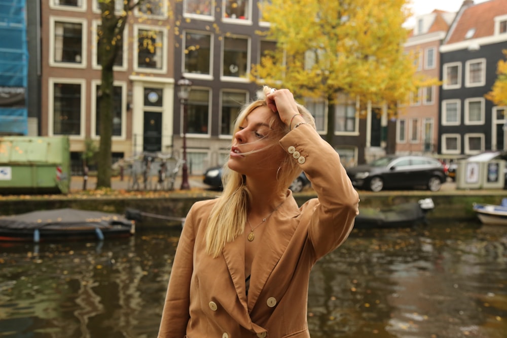 a woman in a tan jacket is standing near a body of water