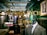 A tailor shop window display featuring a plaid suit on a mannequin, with elegant gold lettering that reads 'Kings Inch Tailor Est. 1943.' Inside the shop, there are neatly organized racks of shirts, jackets, and shoes. The interior has a vintage style with dark wooden shelves and green walls. A framed photograph of a man holding a child's hand adds a personal touch.