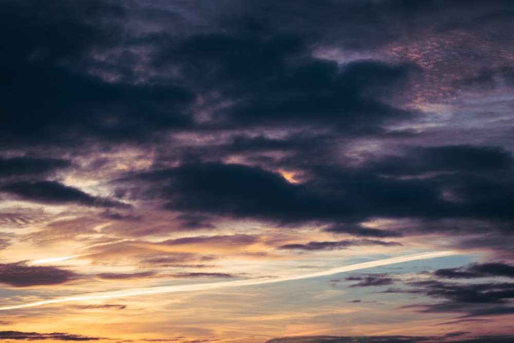 a plane flying through a cloudy sky at sunset