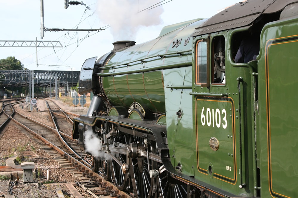 a green train traveling down train tracks next to a train station