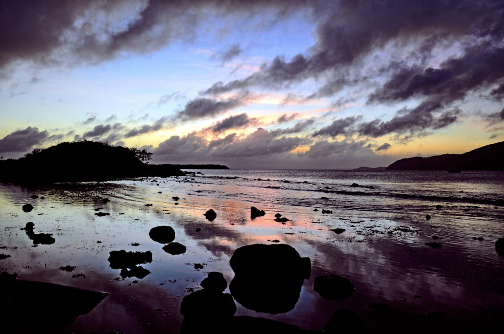 a beach with rocks and water under a cloudy sky