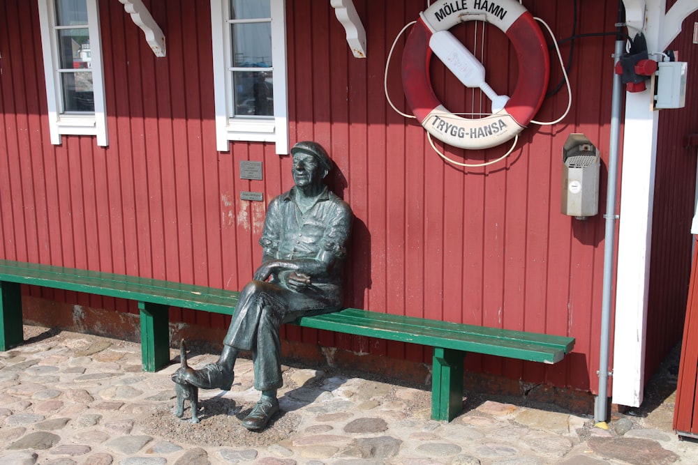 une statue d’un homme assis sur un banc à côté d’un bâtiment rouge