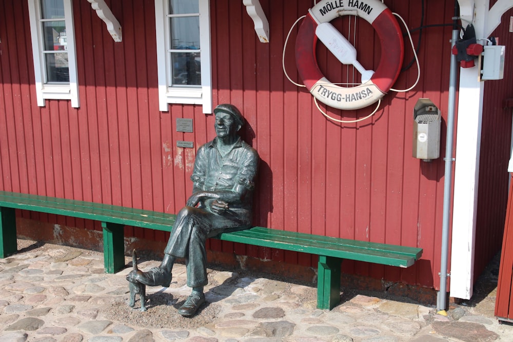 a statue of a man sitting on a bench next to a red building