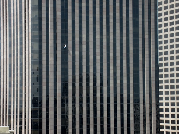 A cordist working on the glass facade of a towering skyscraper in an urban setting.